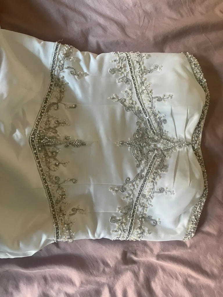 white A-line gown featuring a fitted, subtly ruched bodice with intricate beaded or embroidered detailing at the empire waist.